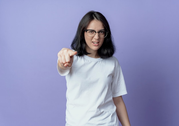 Segura joven bastante caucásica con gafas apuntando a la cámara aislada sobre fondo púrpura con espacio de copia