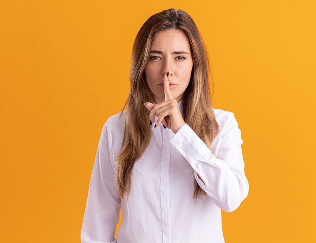 Segura joven bastante caucásica haciendo gesto de silencio aislado en la pared naranja con espacio de copia