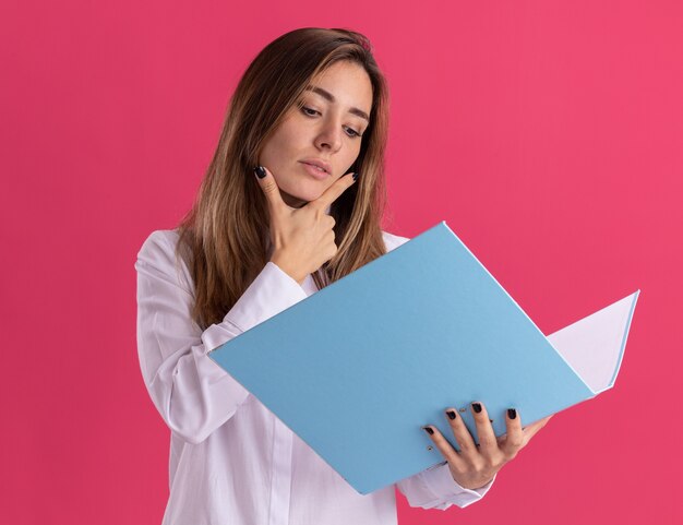 Segura joven bastante caucásica pone la mano en la barbilla sosteniendo y mirando la carpeta de archivos