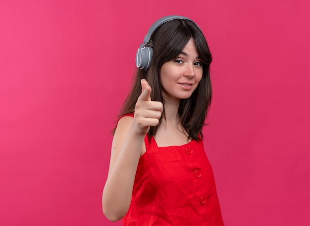 Foto gratuita segura joven caucásica con auriculares apuntando a la cámara sobre fondo rosa aislado con espacio de copia