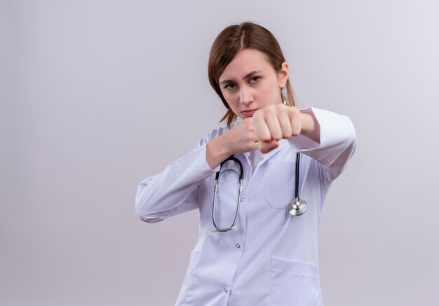 Segura joven doctora vistiendo bata médica y estetoscopio haciendo gesto de boxeo con espacio de copia