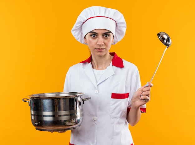 Segura joven hermosa en uniforme de chef sosteniendo una cacerola con cucharón