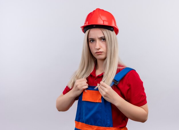 Segura joven rubia ingeniero constructor chica en uniforme poniendo las manos en su uniforme en un espacio en blanco aislado con espacio de copia