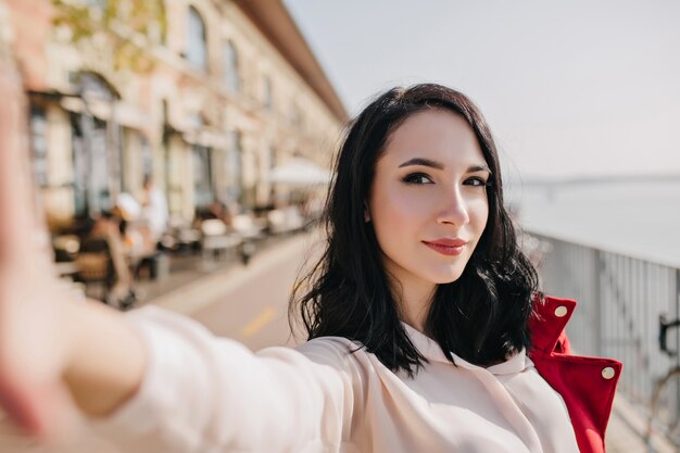 Segura mujer blanca con cabello negro haciendo selfie con expresión de cara interesada