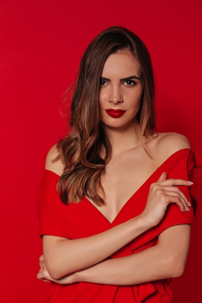 Segura de mujer bonita con cabello ondulado con vestido rojo con labios rojos sobre pared roja