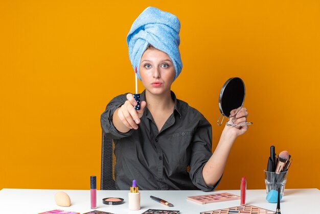 Segura mujer hermosa se sienta a la mesa con herramientas de maquillaje envuelto en cabello