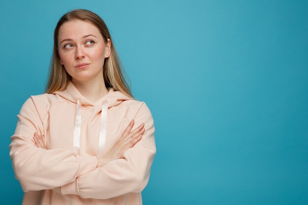 Seguro joven mujer rubia de pie con postura cerrada mirando hacia arriba