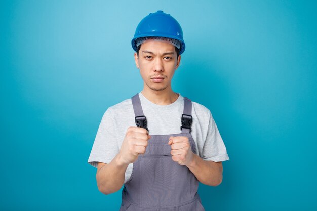 Seguro joven trabajador de la construcción con casco de seguridad y uniforme haciendo gesto de boxeo