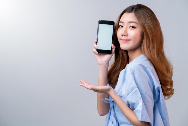 Seguro de negocios saludable hermosa mujer asiática en uniforme de hospital sonrisa con mano muestra ideas de teléfonos inteligentes de pantalla en blanco para un paquete de seguro feliz y promoción con fondo borroso de hospital