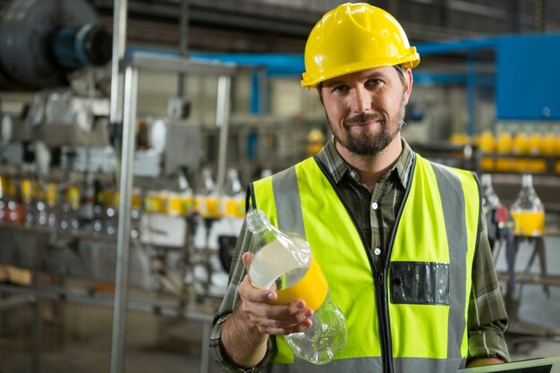 Seguro trabajador masculino inspeccionando botellas en fábrica de jugos