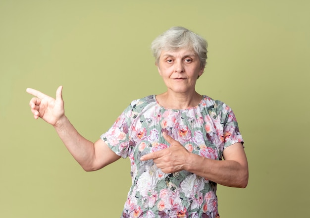 Foto gratuita seguros de anciana apunta al lado con las dos manos aisladas en la pared verde oliva