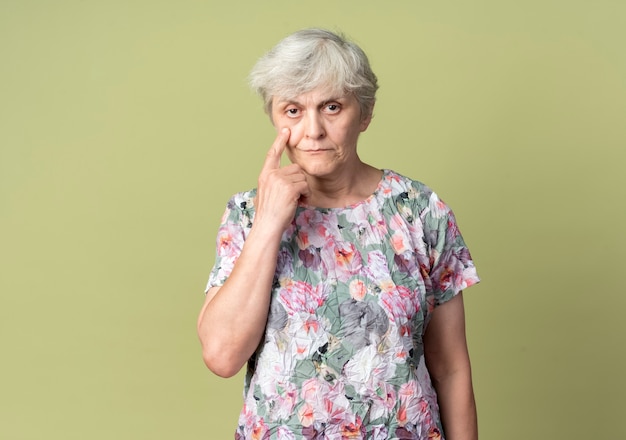 Seguros de anciana apunta a los ojos aislados en la pared verde oliva