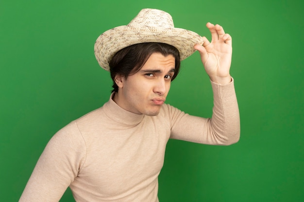 Seguros de chico guapo joven con sombrero con sombrero aislado en la pared verde