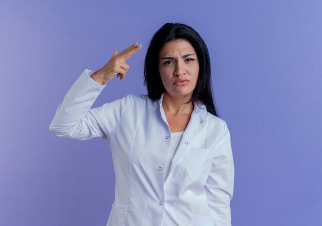 Seguros de joven doctora vistiendo bata médica mirando haciendo gesto de pistola