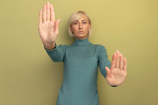 Seguros de mujer bastante rubia eslava gestos dejar de firmar la mano con las dos manos aisladas en la pared verde oliva