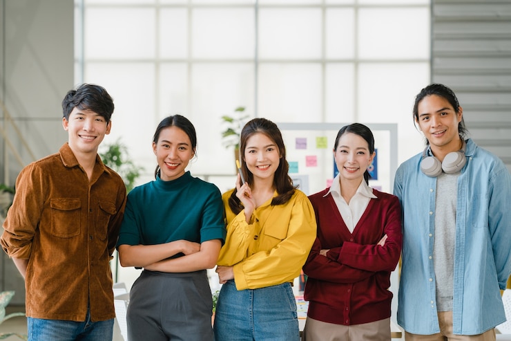 Photo Gratis sekelompok anak muda kreatif asia yang mengenakan pakaian kasual rapi tersenyum dan bersedekap di tempat kerja kantor kreatif. pria dan wanita asia yang beragam berdiri bersama di startup. konsep kerja tim rekan kerja.