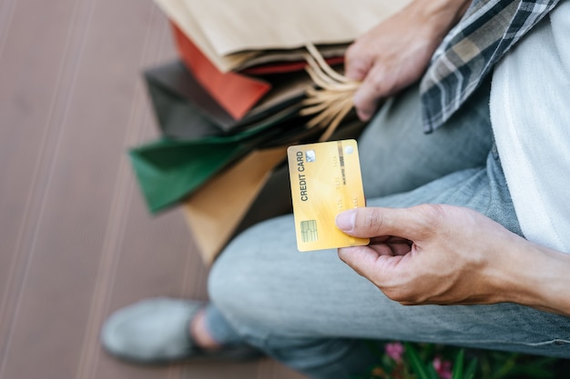 Seleccione la tarjeta de crédito de enfoque en la mano del joven apuesto en máscara, sosteniendo una bolsa de papel