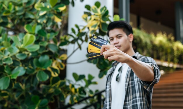 Seleccione la tarjeta de crédito de enfoque en la mano del joven guapo con gafas de sol, sosteniendo una bolsa de papel