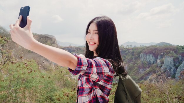 El selfie asiático de la mujer del backpacker encima de la montaña, hembra joven feliz usando el teléfono móvil que toma el selfie disfruta de días de fiesta en la aventura del senderismo.