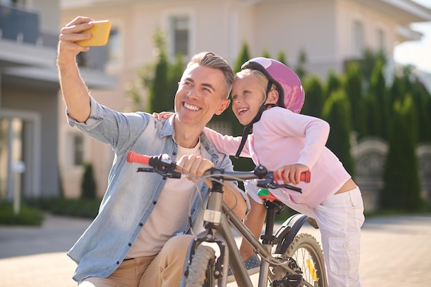 Selfie. Un hombre sonriente haciendo selfie con su hijo en bicicleta