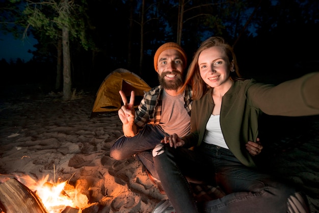 Selfie de pareja acampando en la noche por fogata.