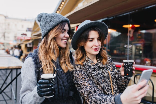 Selfie retrato de mujeres de moda alegres divirtiéndose en la calle soleada de la ciudad. Aspecto elegante, divertirse, viajar con amigos, sonreír, expresar verdaderas emociones positivas.