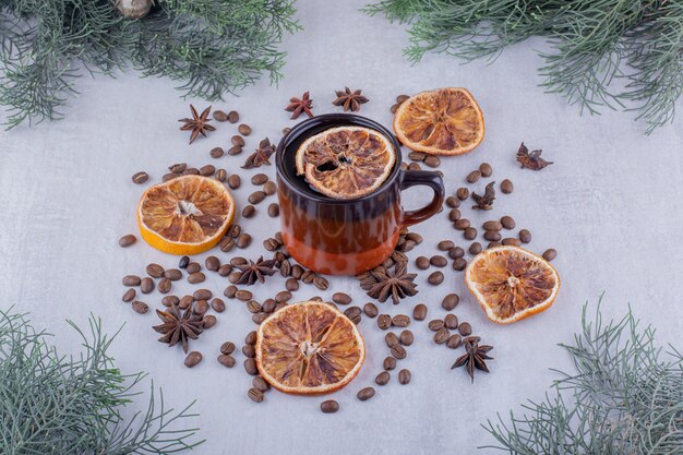 Semillas de anís esparcidas, rodajas de naranja secas y una taza de té sobre fondo blanco.