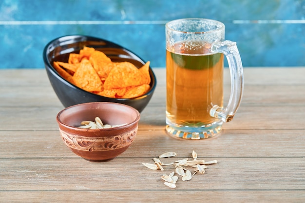 Semillas de girasol, un tazón de patatas fritas y un vaso de cerveza en la mesa de madera.