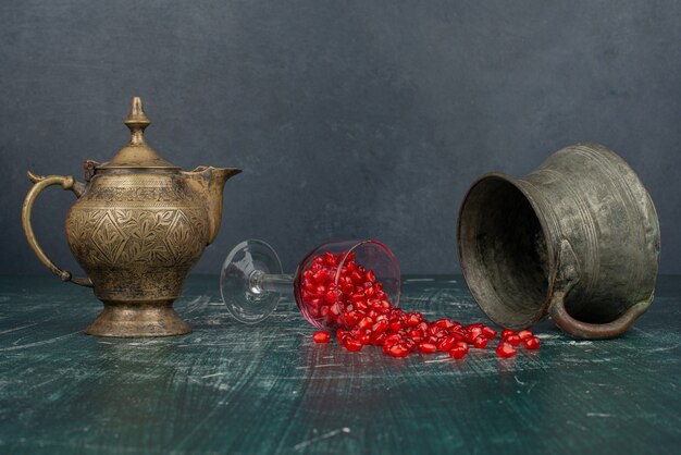 Semillas de granada esparcidas sobre una mesa de mármol con jarrón y tetera.