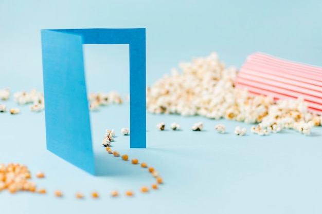 Semillas de maíz pasando por una puerta de papel azul que se convierte en palomitas de maíz sobre un fondo azul