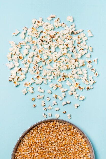 Semillas de palomitas de maíz en un recipiente con palomitas de maíz sobre fondo azul