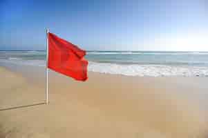 Foto gratuita señal de advertencia de una bandera roja en una hermosa playa con un cielo azul y un mar turquesa