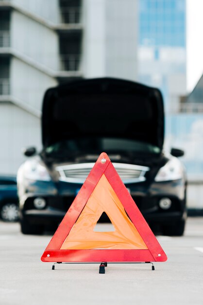 Señal de emergencia con coche negro en segundo plano.