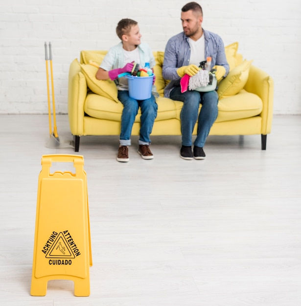 Foto gratuita señal de piso mojado con hombre y niño en el sofá