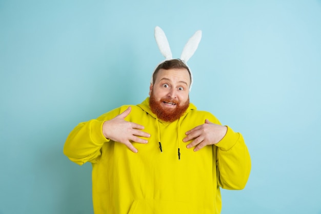 Señalando a sí mismo. Hombre caucásico como un conejito de Pascua con ropa casual brillante sobre fondo azul de estudio.