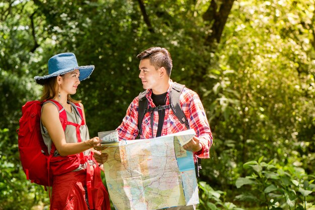 Senderismo - excursionistas mirando el mapa. Pareja o amigos navegando juntos sonriendo feliz durante la excursión de camping al aire libre en el bosque. Joven mujer de raza mixta asiática y el hombre.