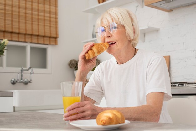 Senior comiendo un croissant en la cocina