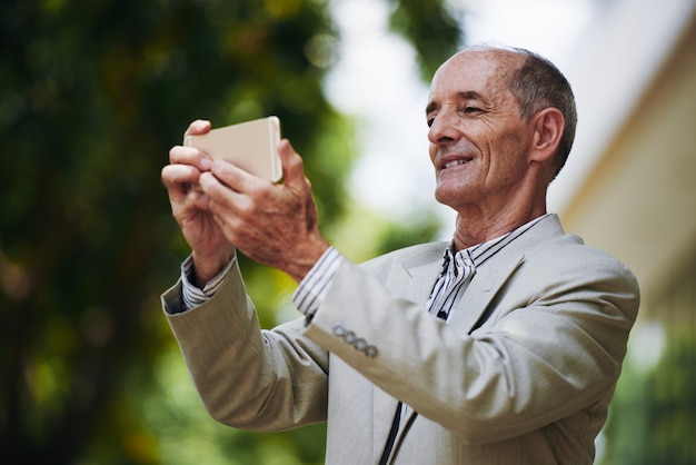 Senior empresario caucásico en traje takin selfie con smartphone al aire libre