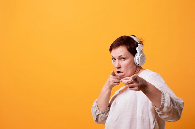 Senior femenino con auriculares señalando