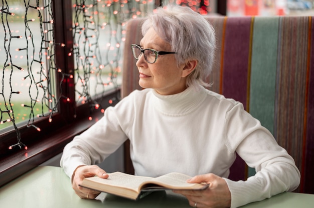 Senior femenino con libro mirando por la ventana