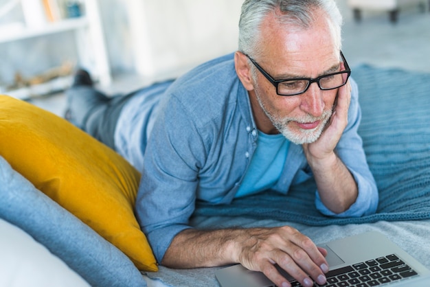 Senior hombre acostado en la cama usando la computadora portátil