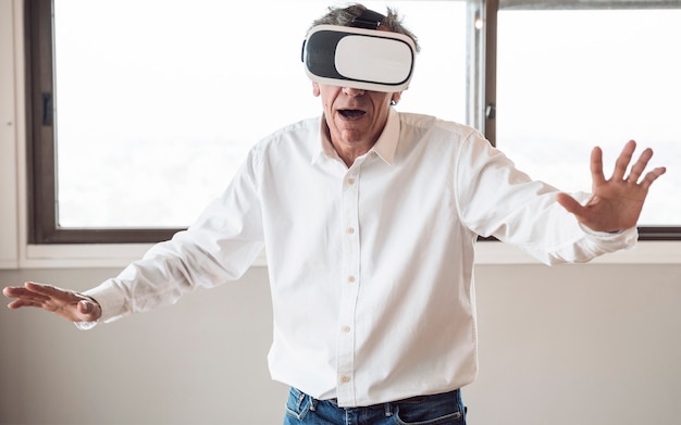 Senior hombre en camisa blanca usando un casco de realidad virtual en la habitación