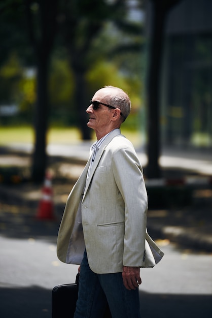 Senior hombre caucásico en gafas de sol y blazer caminando en parque urbano