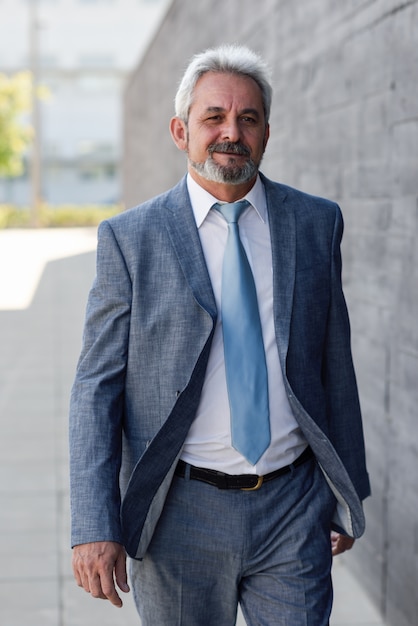 Senior hombre de negocios caminando fuera del edificio de oficinas moderno.