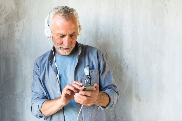 Foto gratuita senior hombre de pie delante de muro de hormigón escuchando música en auriculares