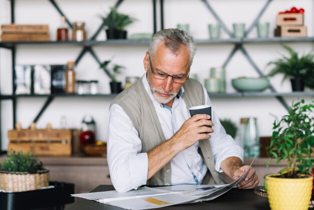 Senior hombre sosteniendo una taza de café leyendo el periódico en casa