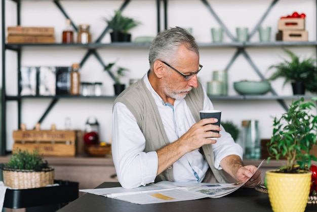 Senior hombre sosteniendo la taza de café en la mano leyendo el periódico