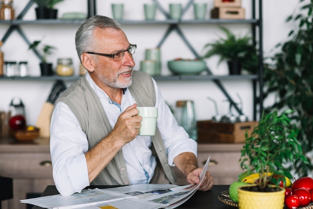 Senior hombre sosteniendo una taza de café y periódico mirando a otro lado