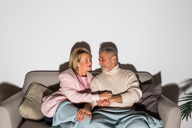 Senior hombre tomados de la mano con mujer y viendo la televisión en el sofá