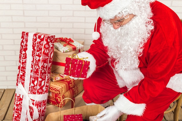 Senior hombre en traje de Santa Claus poniendo regalos en bolsa kraft